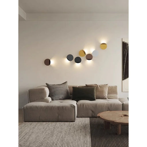 Modern artistic wall lamp on beige living room wall above sectional sofa and round coffee table.