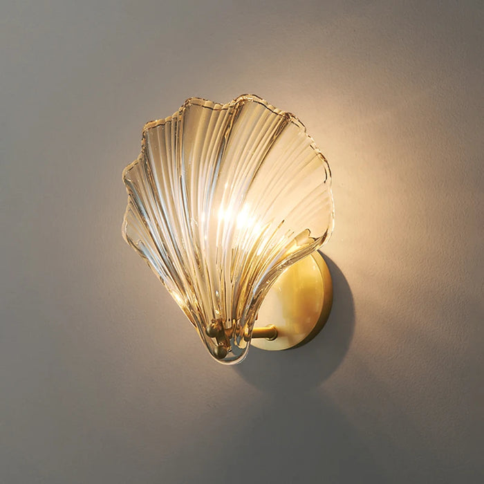 Modern luxury brass shell wall lamp with clear glass shade, elegant lighting fixture for contemporary interiors.