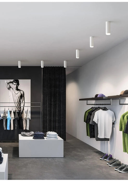 Modern retail space with long tube LED ceiling lamps illuminating clothing displays and wall art.