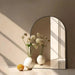 modern arched mirror with aluminum frame reflecting vases with flowers in a sunlit room