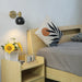 Modern adjustable LED wall lamp with long arm illuminating cozy bedroom decor with wooden bed and sunflower arrangement.