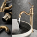 Antique brass long neck basin faucet with ceramic valve, deck-mounted design, and water flow into a stone basin.