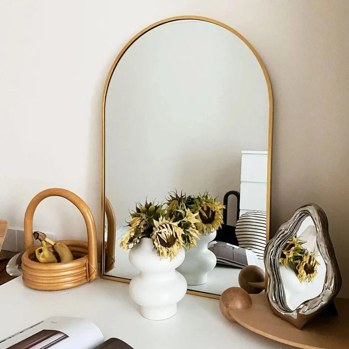 Elegant large arch mirror with aluminum frame reflecting stylish room decor including flowers and baskets.