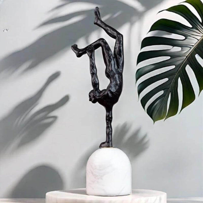 Giacometti inspired abstract metal sculpture on marble base with leaf shadow background.