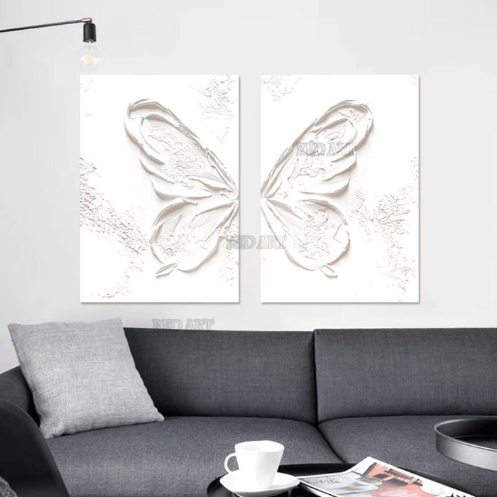 Two-piece white abstract butterfly oil painting displayed above a modern gray sofa, enhancing the room's minimalist decor.